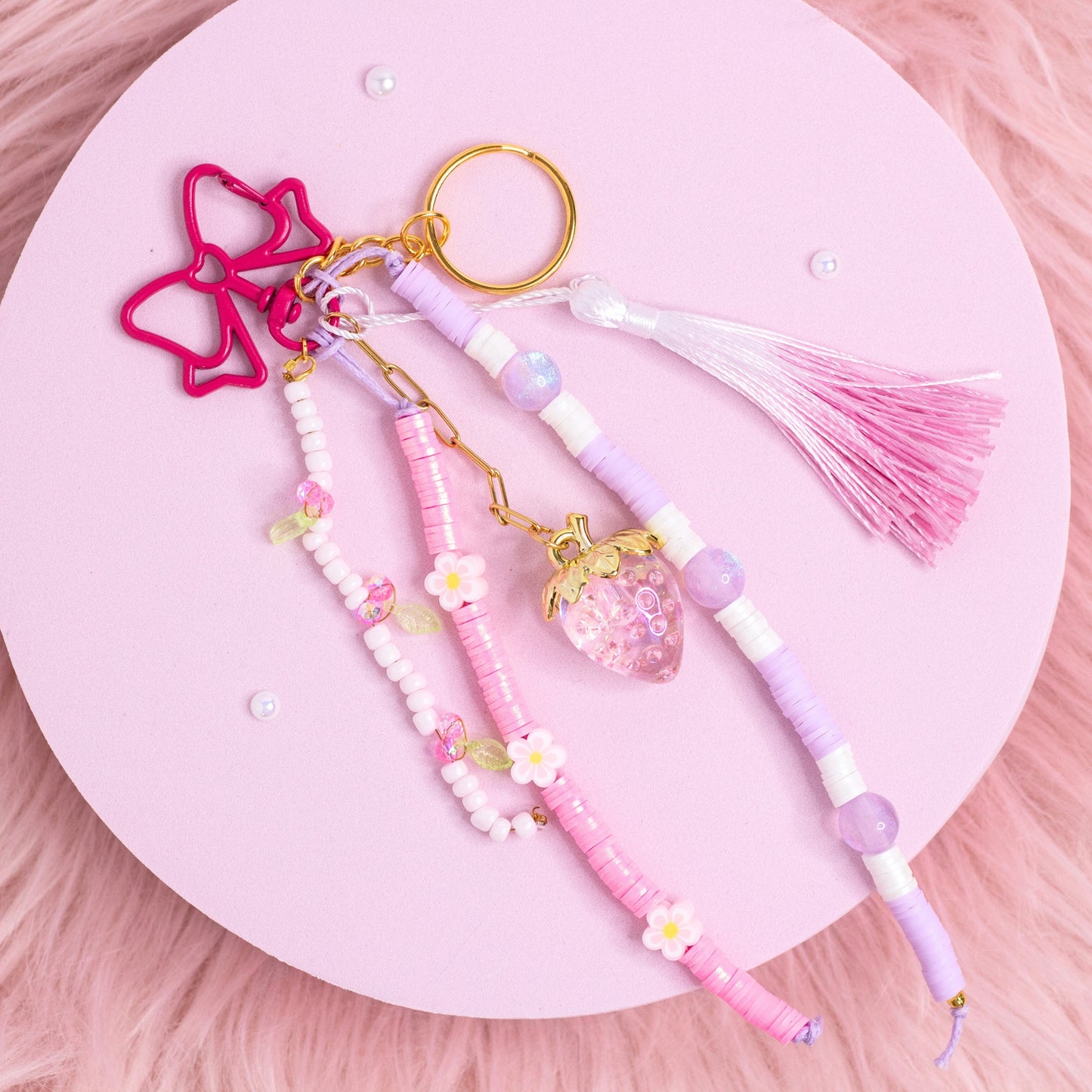 Handmade strawberry beaded purse charm keychain with pastel pink and lavender beads and strawberry pendant on pink background
