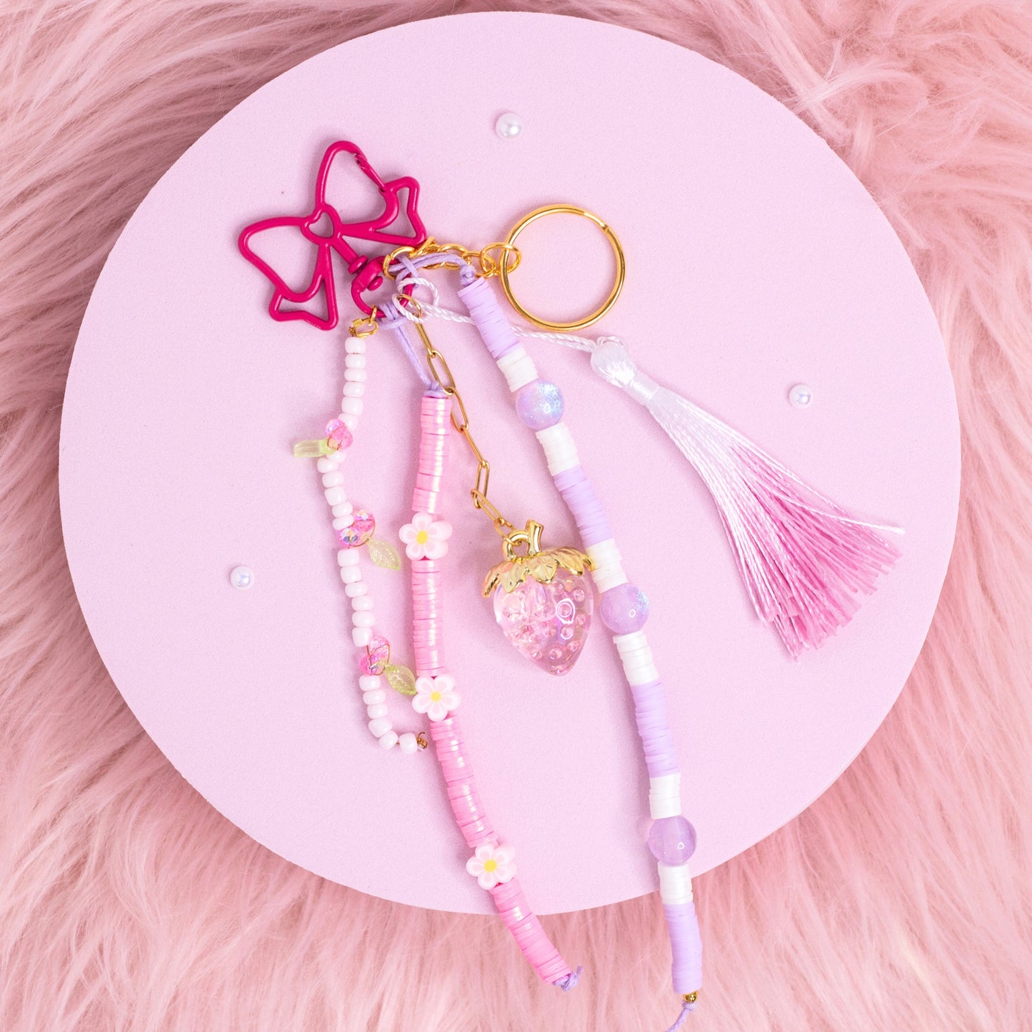 Strawberry purse charm keychain with pink and purple beads, daisy accents, and bow clip displayed on pink aesthetic background