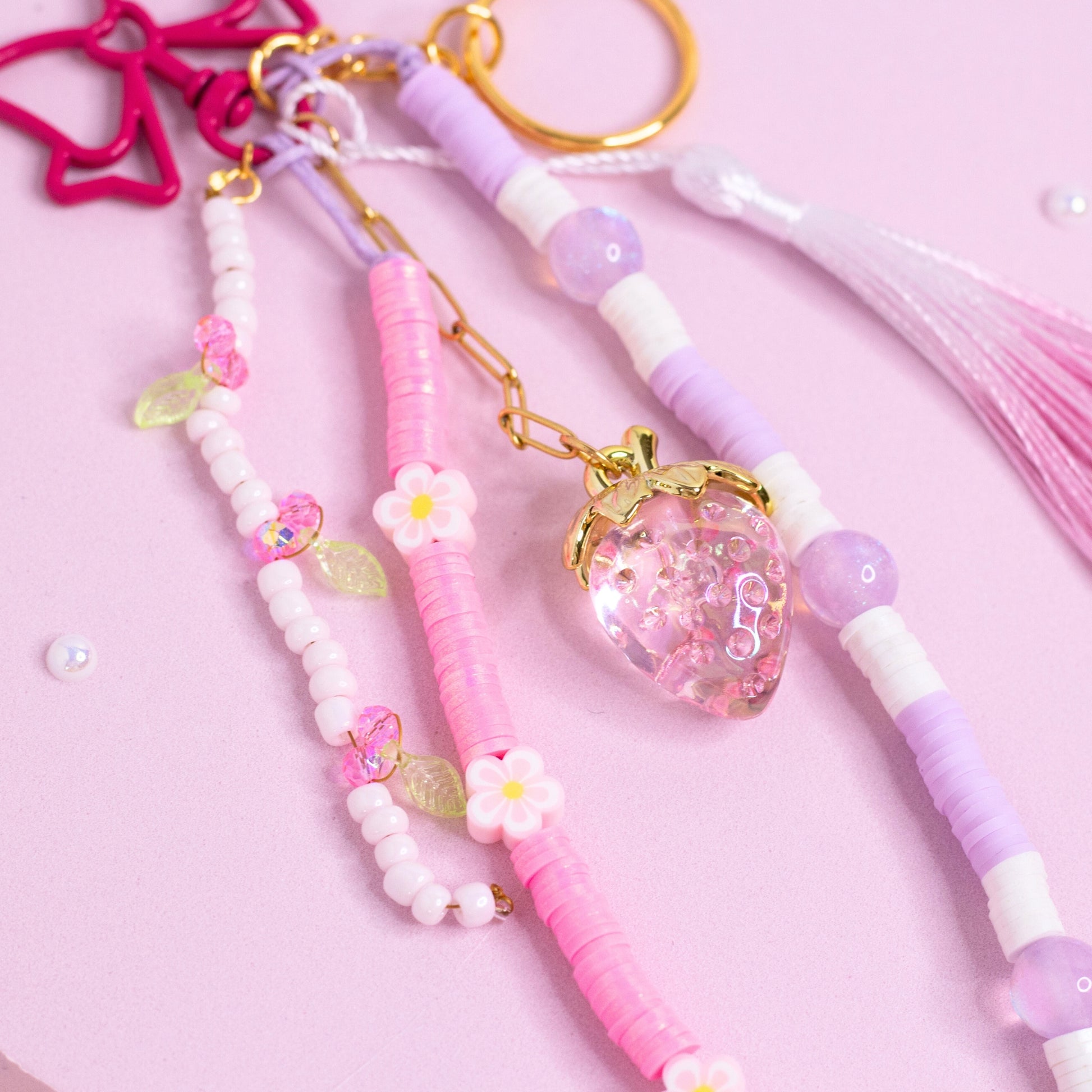 Close-up of strawberry beaded purse charm keychain with pink beads, floral accents, and strawberry charm on soft pink background