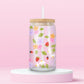 Glass can tumbler with bamboo lid and glass straw featuring strawberries, daisies, pastel flowers, green leaves, ladybugs, and lavender bow details on a pink background.