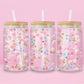 Glass can tumbler with bamboo lid and glass straw featuring a pastel floral, mushroom, blueberry, bow, and heart design on a pink background.