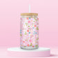 Glass can tumbler with bamboo lid and glass straw featuring a pastel floral, mushroom, blueberry, bow, and heart design on a pink background.