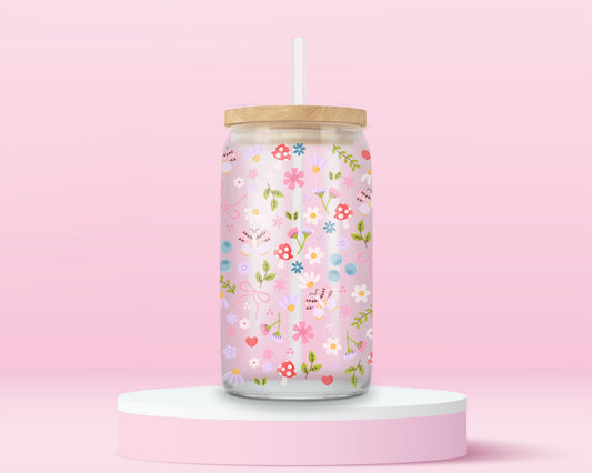 Glass can tumbler with bamboo lid and glass straw featuring a pastel floral, mushroom, blueberry, bow, and heart design on a pink background.