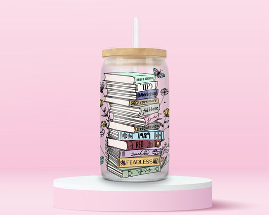 glass tumbler with stacked books labeled Taylor Swift albums like Fearless, Red, 1989, Folklore, Midnights, surrounded by flowers and butterflies.