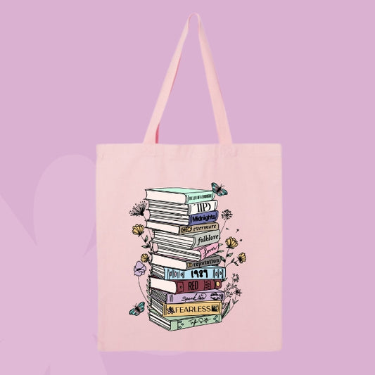 Pink tote bag with a tall stack of books labeled with Taylor Swift album names, surrounded by flowers and butterflies.