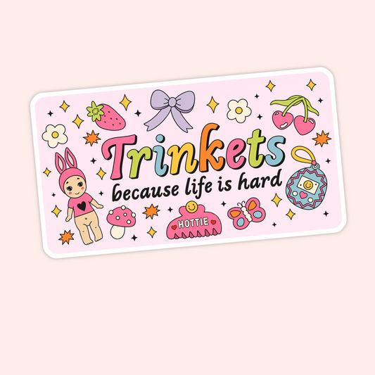 Cute pink sticker that says “Trinkets because life is hard” with colourful doodles including cherries, a bow, strawberry, butterfly, mushroom, and charm.