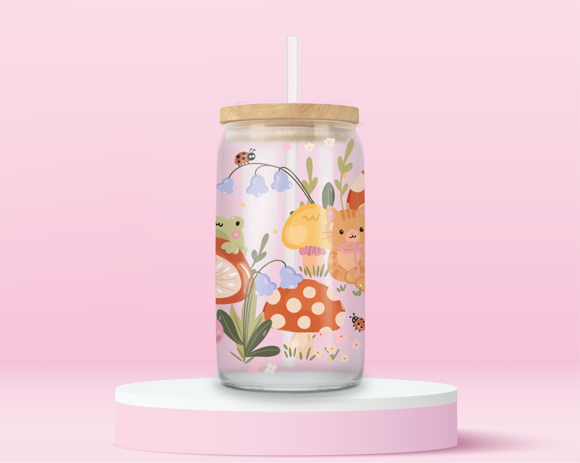 Glass can tumbler with bamboo lid and glass straw featuring an orange cat, mushrooms, bluebell flowers, ladybugs, leafy stems, and woodland cottagecore illustrations on a pink background.