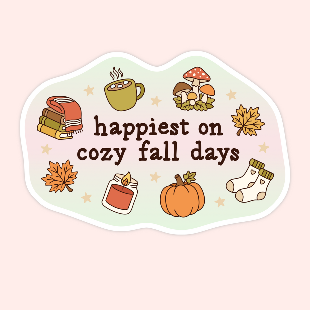 A die-cut sticker with a wavy border featuring autumn illustrations and the text 'happiest on cozy fall days' in dark brown lettering, shown on a pale pink background.