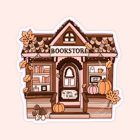 A die-cut sticker featuring a cute autumn-themed illustration of a cozy bookshop. The pink and brown storefront has scalloped roof tiles, a sign reading 'BOOKSTORE' above the door, pumpkins on the porch, hanging orange leaves, mushrooms, and a ghost in the window.