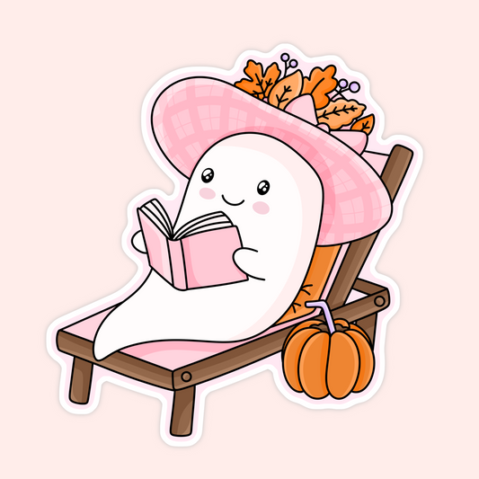 Cute ghost sticker featuring a little ghost reading a pink book while lounging on a chair with a pink hat, autumn leaves and a pumpkin.