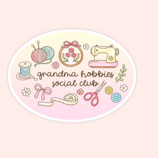 An oval sticker or decal featuring a retro-style illustration of sewing and crafting items, including yarn balls, a sewing machine, scissors, a measuring tape, flowers, and buttons, with the text 'grandma hobbies social club' in brown script. The sticker is centered on a pale pink background.