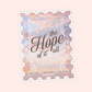 Pastel postage stamp style sticker with a dreamy ocean sunset, ornate white border and “The Hope Of It All” typography