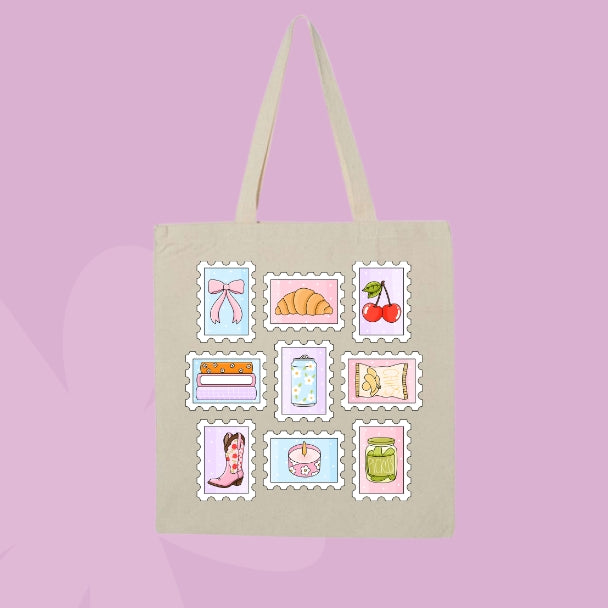 A beige canvas tote bag with two shoulder straps, featuring a grid of nine pastel-colored postage stamp illustrations on the front. The designs include a pink bow, a croissant, cherries, books, a polka-dot jar, a map, cowboy boots, a cupcake, and a green jar, set against a solid pink background.