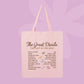 A light pink canvas tote bag with pink handles, featuring a vintage-style printed graphic titled 'The Great Divide: The Last of the Bugs' with a list of bugs and small illustrations, set against a solid lavender-purple background.