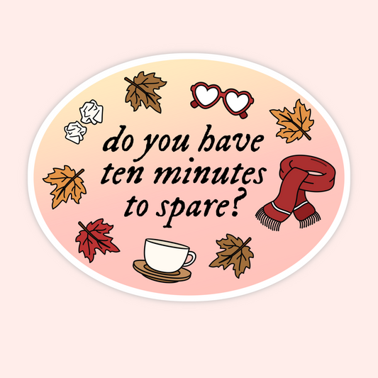 An oval sticker with a pastel gradient background featuring the text 'do you have ten minutes to spare?' in black script. The design includes autumn-themed illustrations such as leaves, a red scarf, heart-shaped glasses, crumpled paper, and a coffee cup on a light pink and peach gradient.