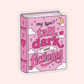 A die-cut sticker shaped like a pink hardcover book with the phrase 'my type? tall, dark and fictional' in stylized lettering, decorated with clouds, hearts, stars, and a crescent moon on a pale pink background.