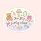 An oval sticker or decal featuring a western-themed 'Thrifty Girly Club' design on a pale pink background. The sticker illustration includes a teddy bear, cowboy boots, a lamp, a mirror, flowers, a stack of books, a teacup, and a pink bow.
