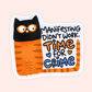A die-cut sticker featuring a cartoon cat with a black head and orange striped body, next to the text 'MANIFESTING DIDN'T WORK. TIME FOR CRIME' in black, orange, and blue lettering, shown on a pale pink background.