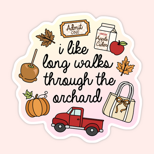 A die-cut sticker with a scalloped edge featuring autumn-themed illustrations and the phrase 'i like long walks through the orchard' in black script. The design includes a caramel apple, pumpkin, red pickup truck, tote bag, apple, admit one ticket, and a carton of apple cider on a pale pink background.